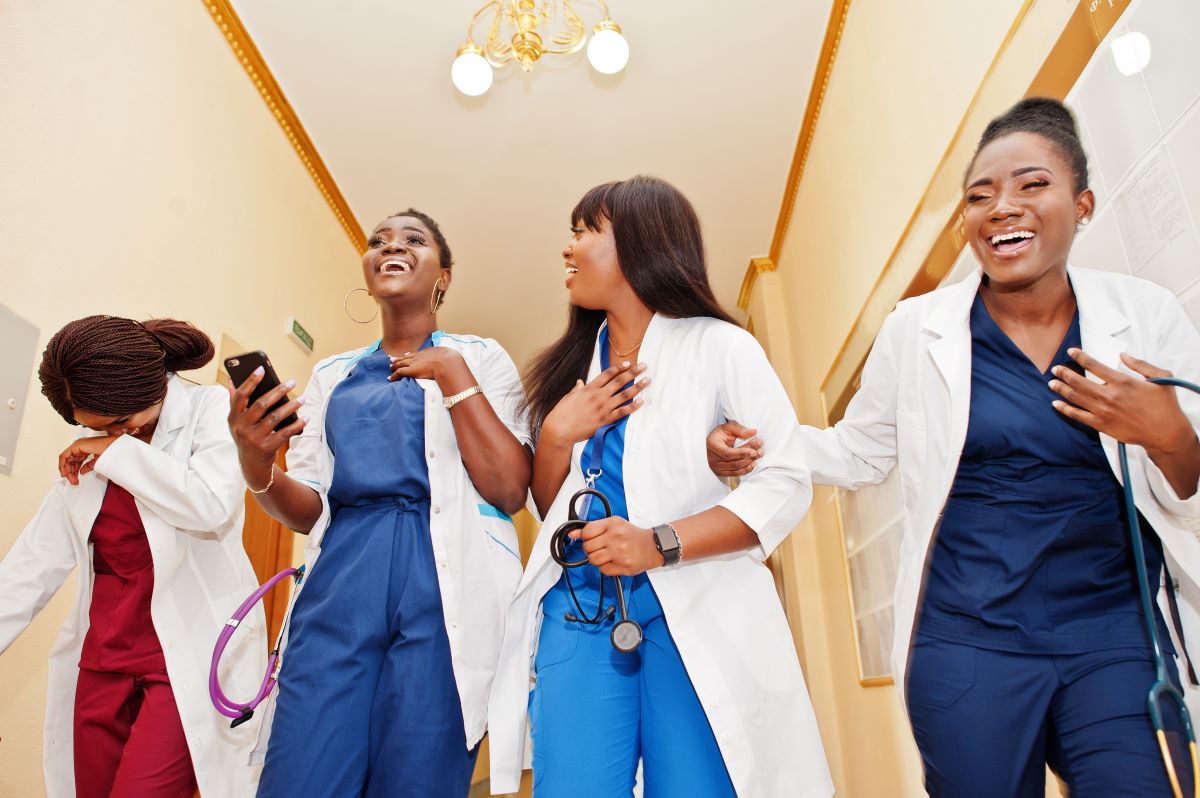 Four nurses, walking down a hallway and laughing together.