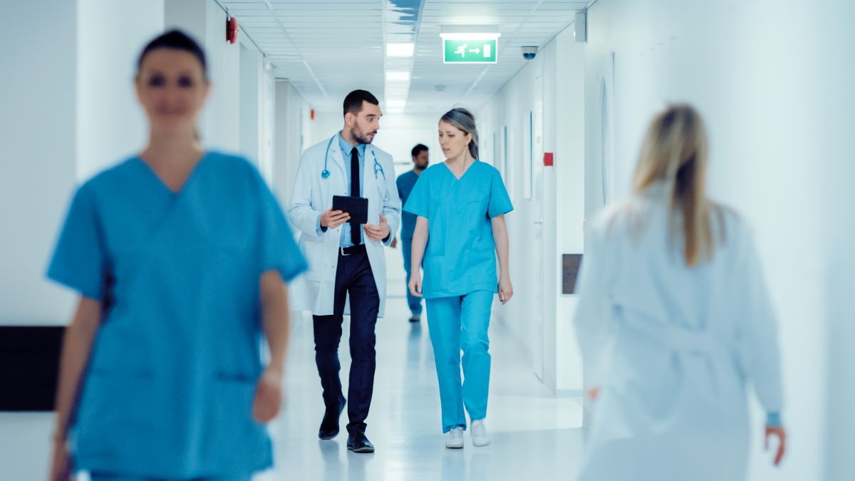 A physician talks to a newly hired nurse in a hospital hallway.