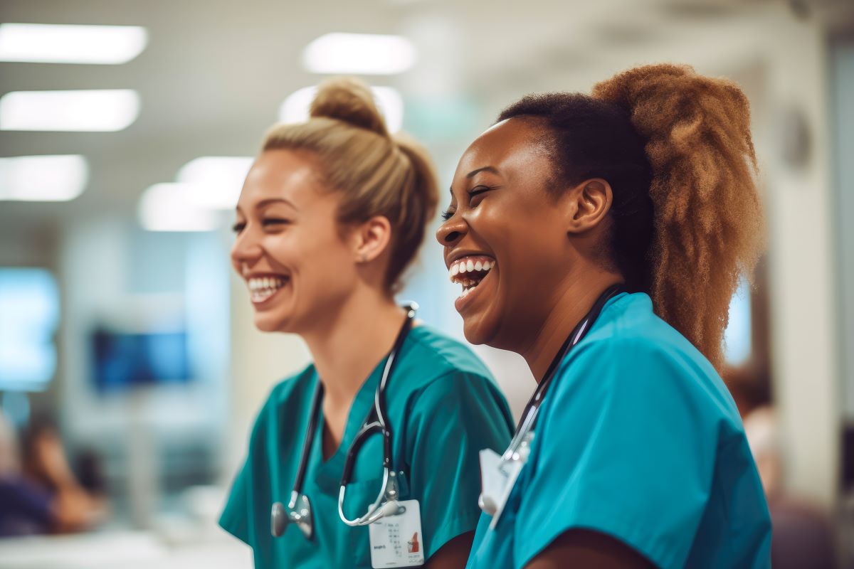 Two nurses, smiling while sharing a moment in the hallway.