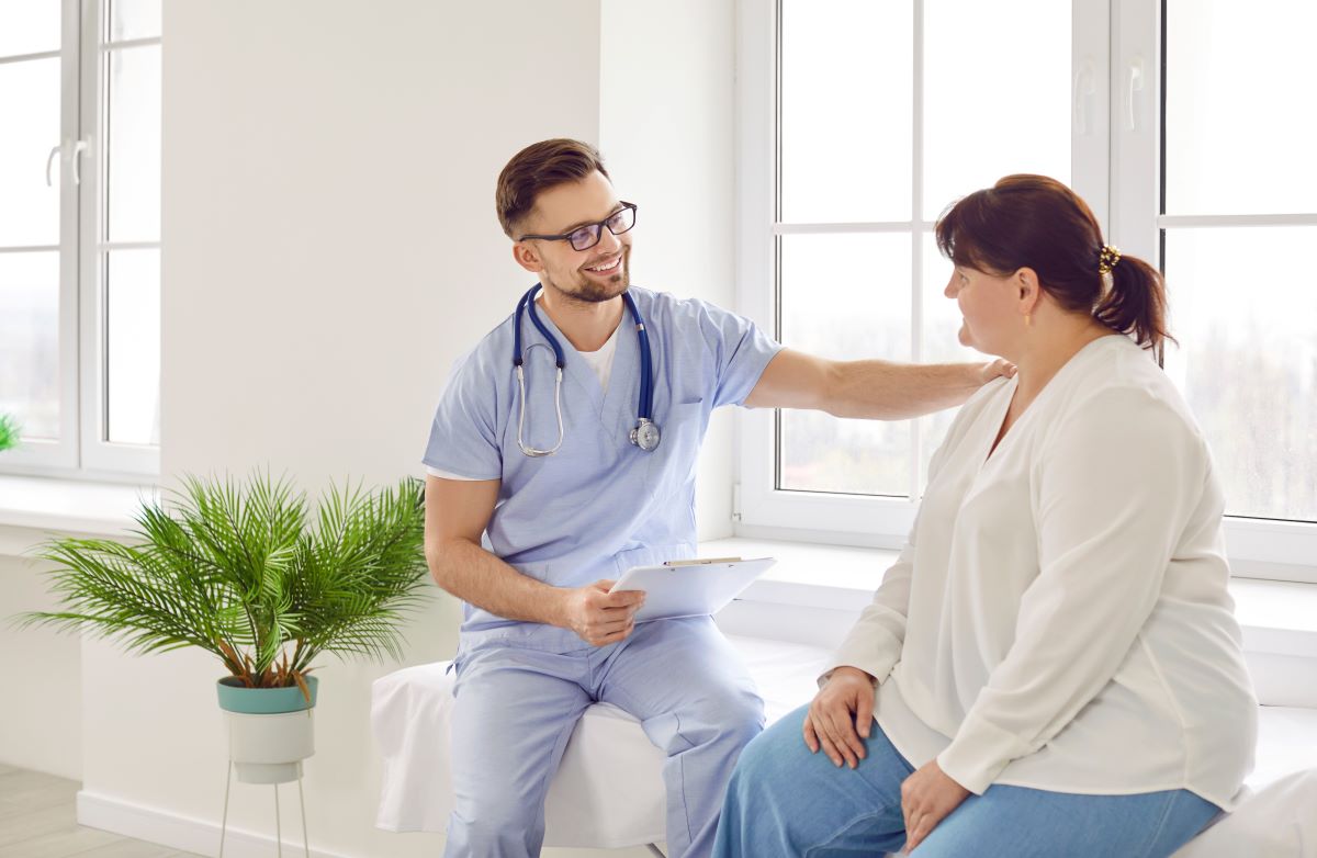 A nurse puts his hand on a patient's shoulder as they discuss her treatment plan.