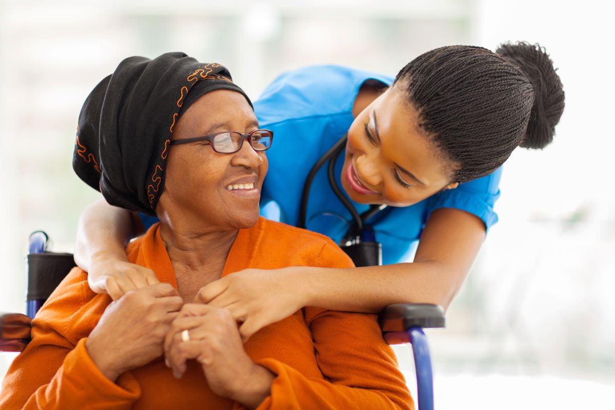 A nurse embraces her patient, who is in a wheelchair.