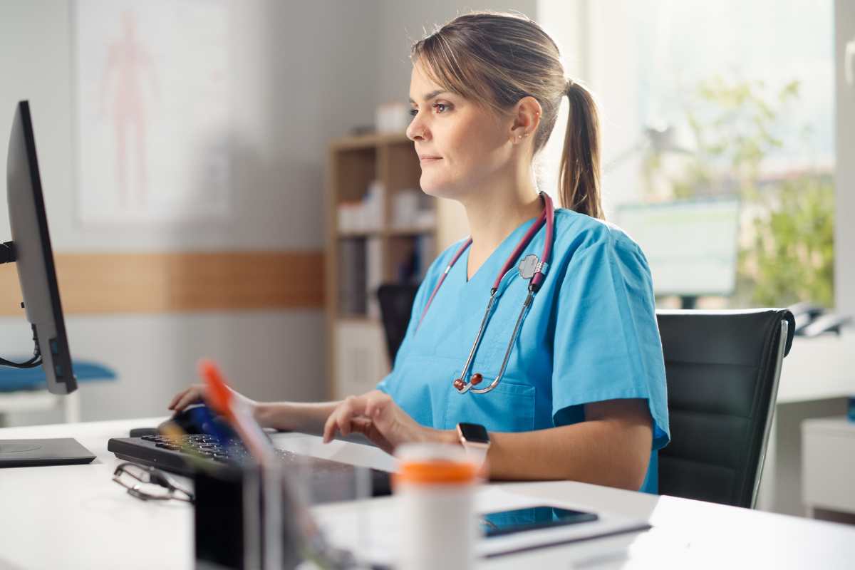 Nurse in scrubs typing her ICU nurse cover letter at a desktop computer