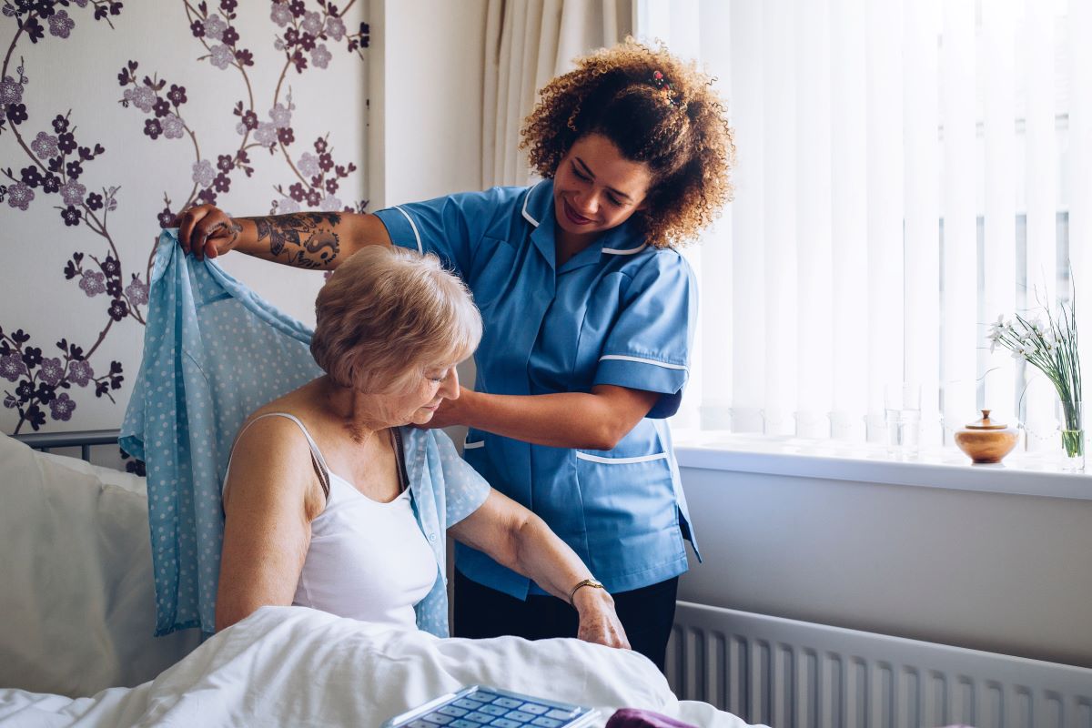 A nurse helps a resident put her shirt on.