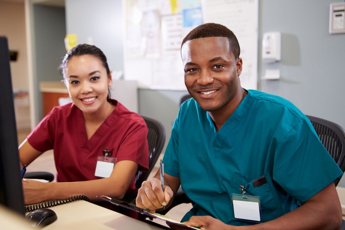 Two nurses at a desk, looking at the camera.