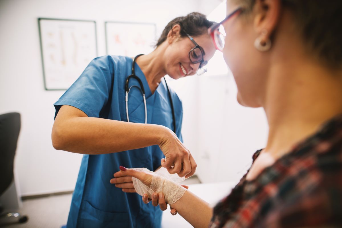 A wound care nurse wraps a bandage around a patient's wrist.