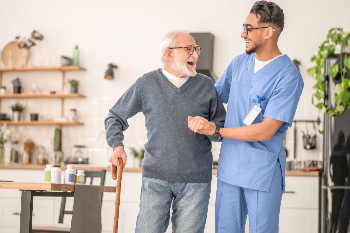 A nurse helps an elderly resident walk with a cane.