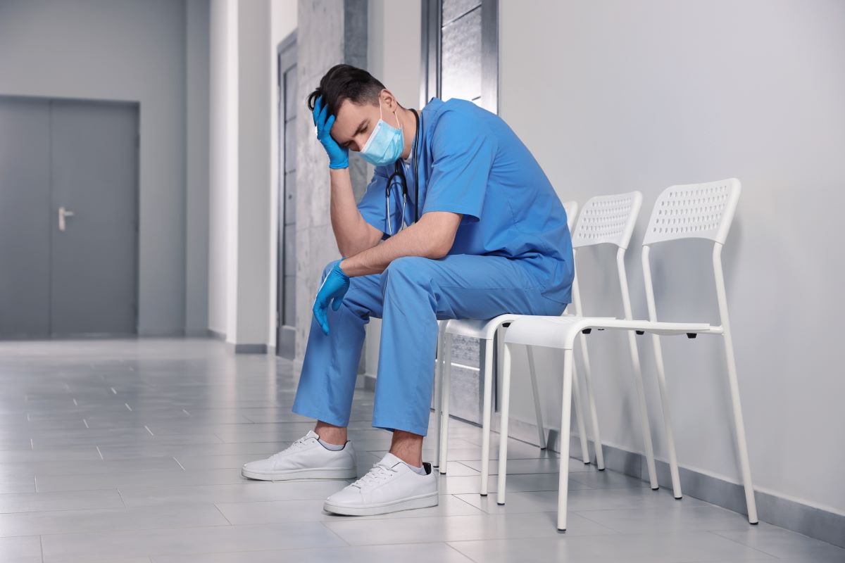 A visibly exhausted and probably burned-out nurse sits on a chair in the hospital's hallway.