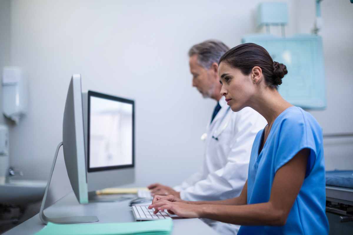 Nurse in scrubs typing a telemetry nurse cover letter on a computer.