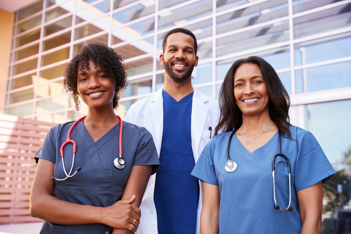 A group of three nurses poses for a picture outside of their facility.