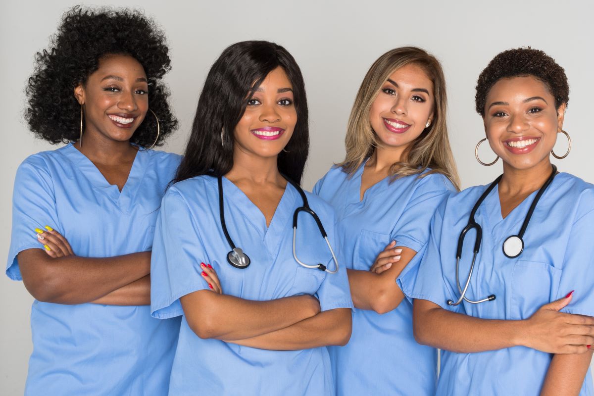 A group of four nurses stands and smiles for the camera.