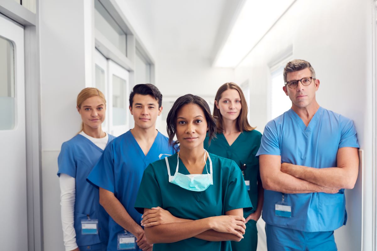 A team of nurses stands in the hallway and looks at the camera.