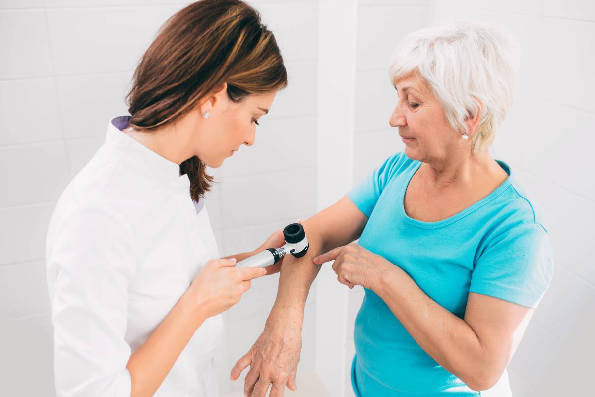 A dermatology nurse practitioner examines a mole on a patient's arm.