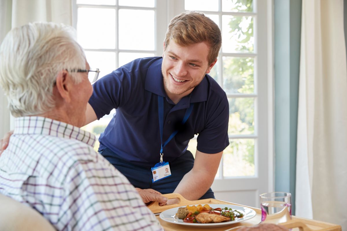 A home health nurse assists his patient with a meal.