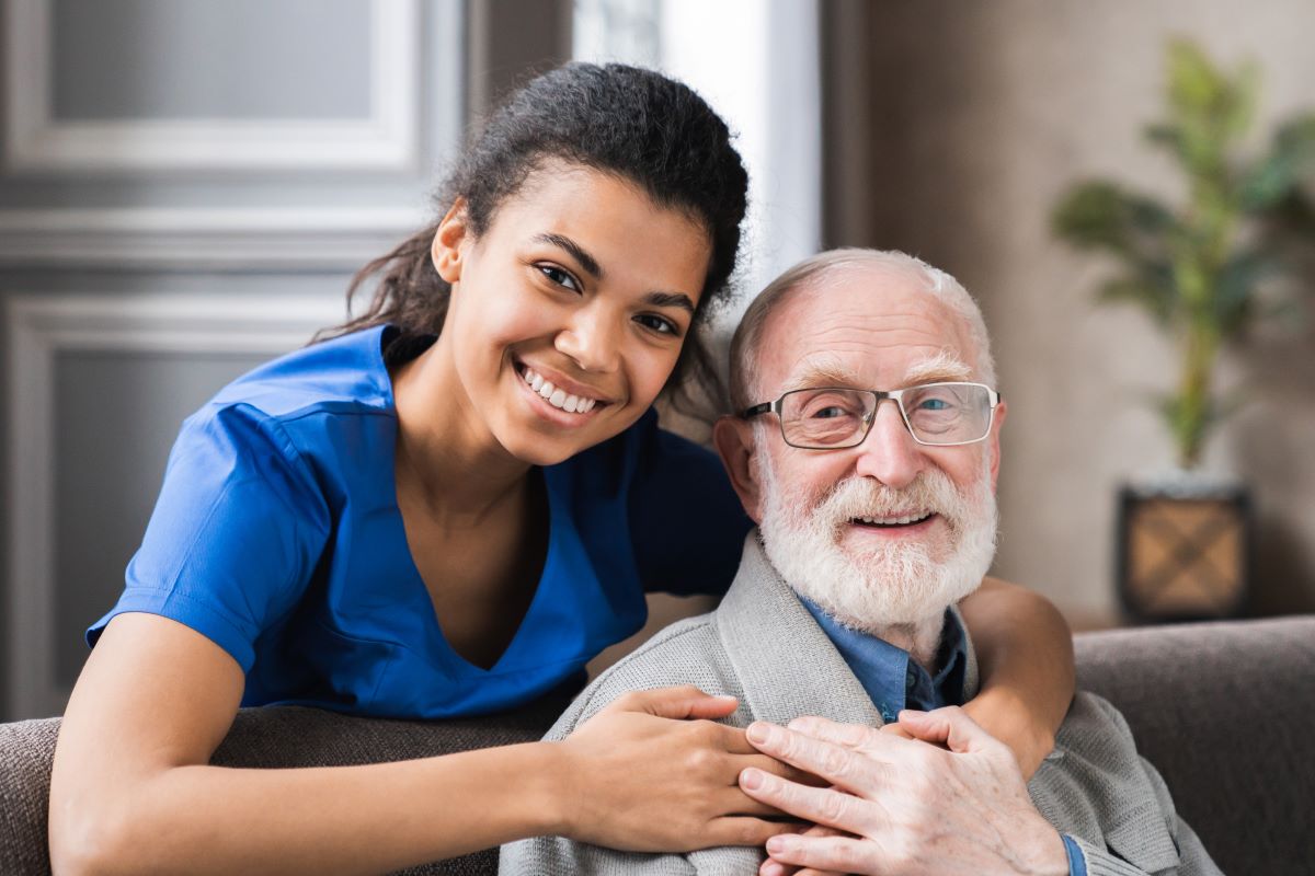 A nurse and a nursing home resident smile at the camera.