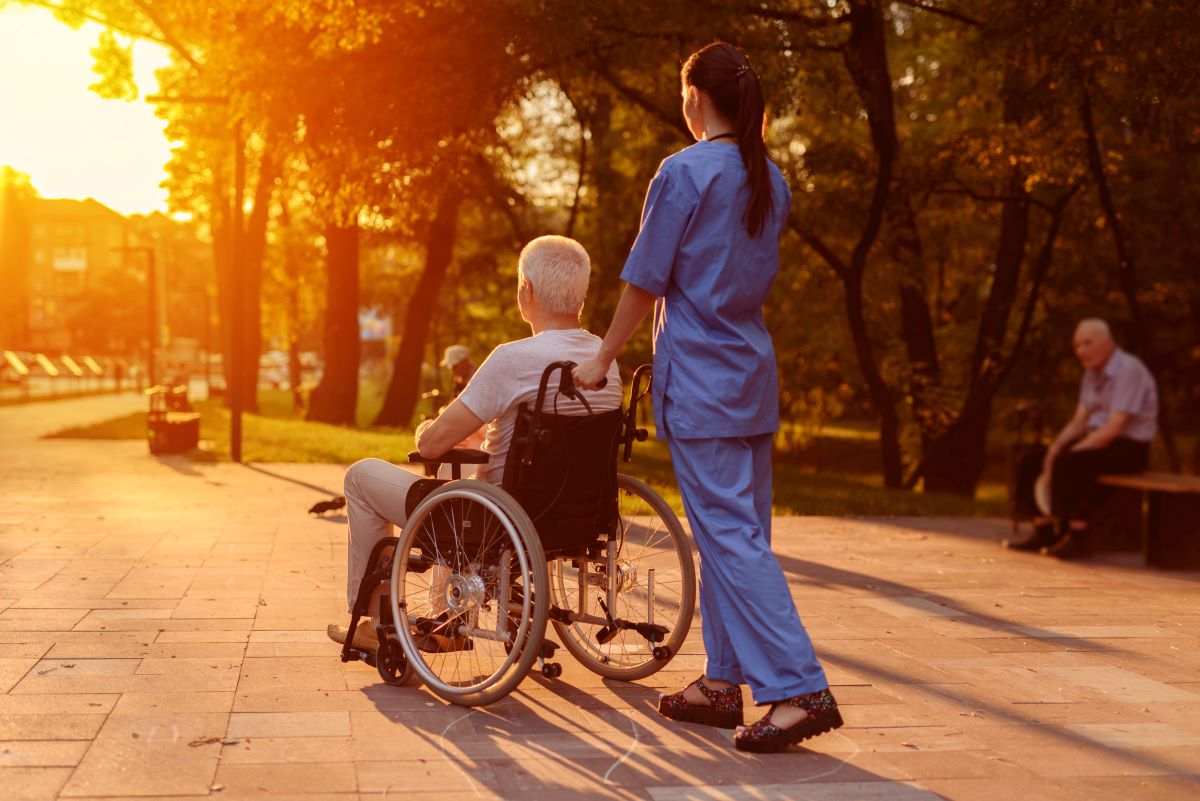 A nurse assists a wheelchair-bound resident outside the facility.