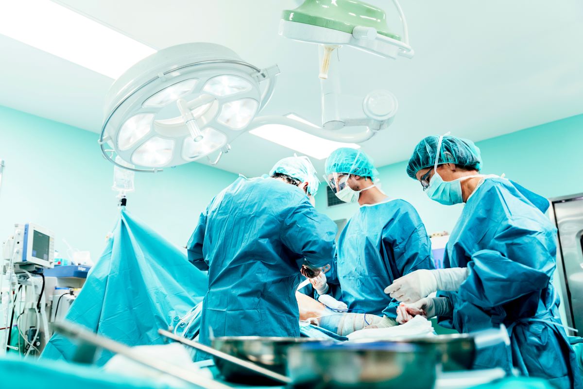 Image of an operating room with a surgery in progress, including a patient surrounded by a surgeon and surgical technologist