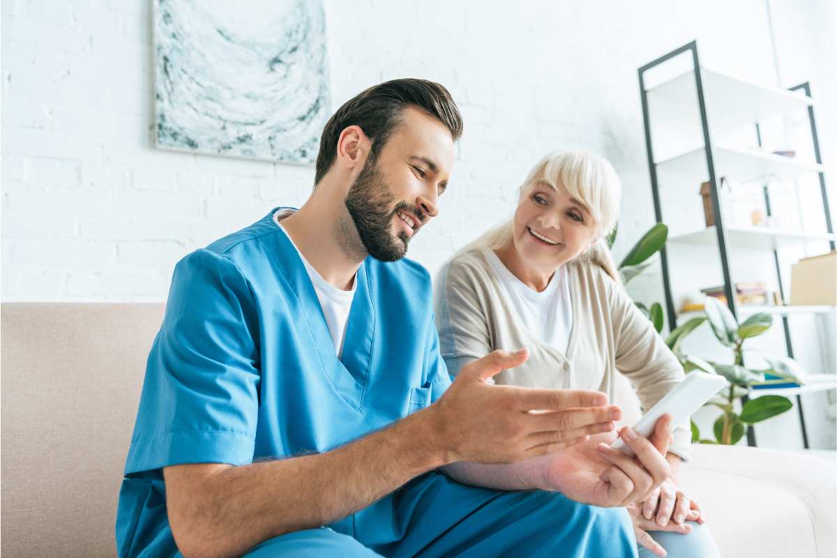 Nurse showing tablet to a patient while sitting on a couch.