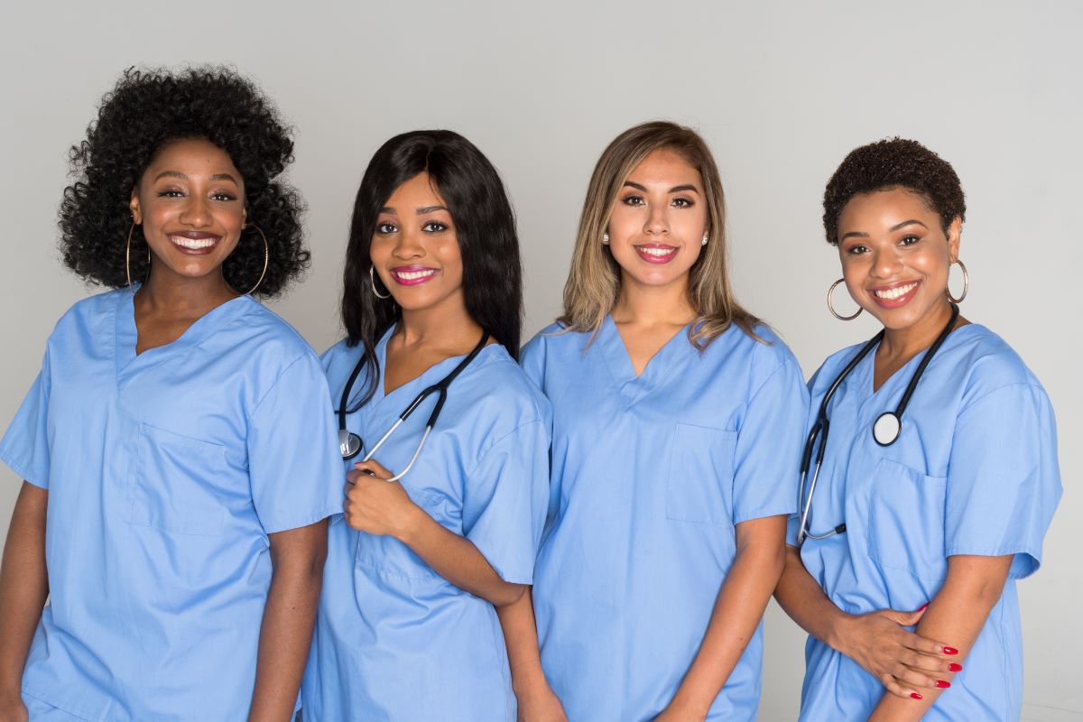 A group of four nurses pose for the camera, smiling.