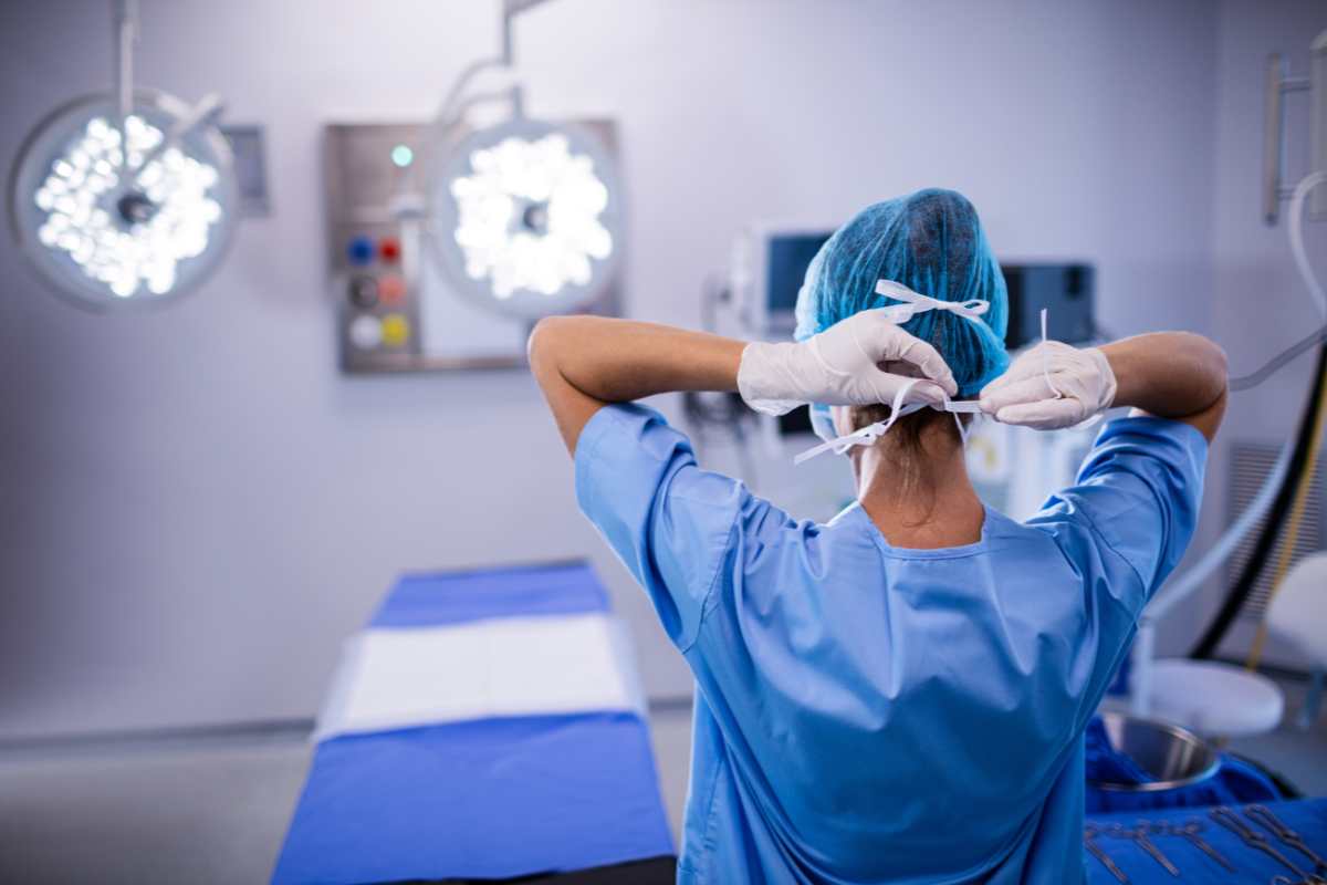 Perioperative nurse in an operating room securing her face mask.