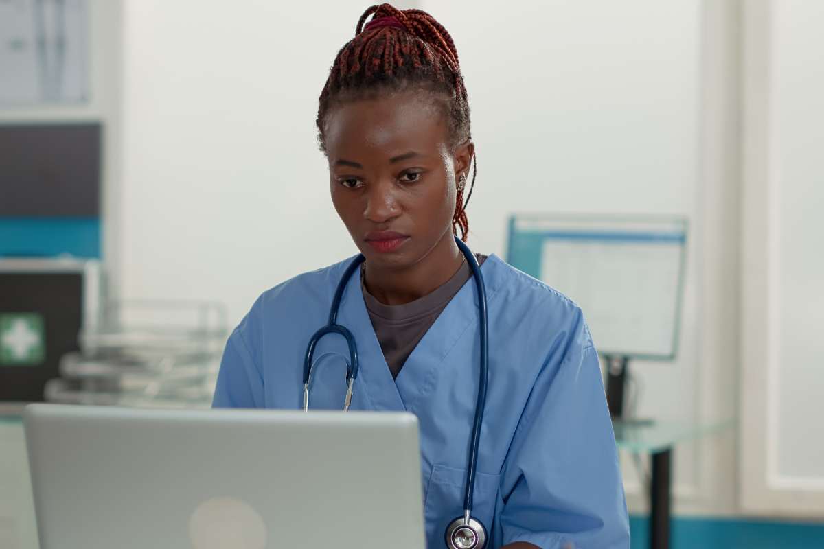 Nurse in scrubs on a laptop typing her PMHNP resume for a job.