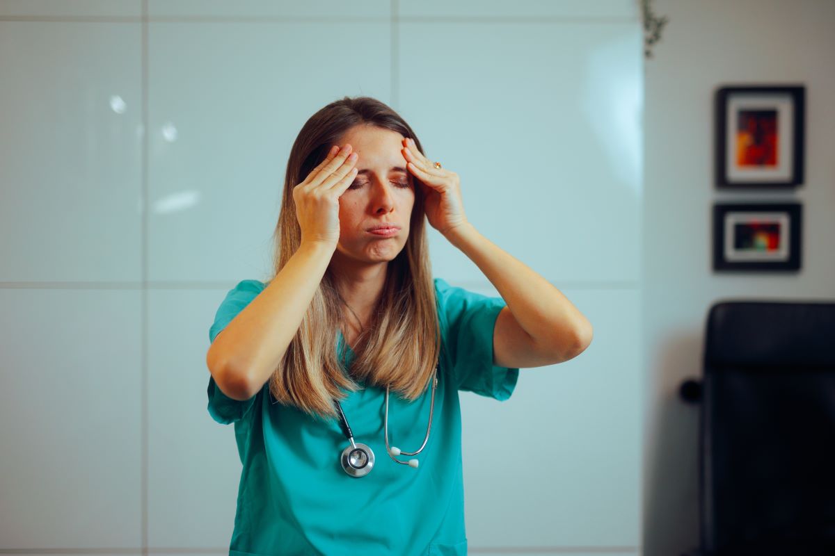 An overworked nurse applies pressure to her head as she deals with stress.