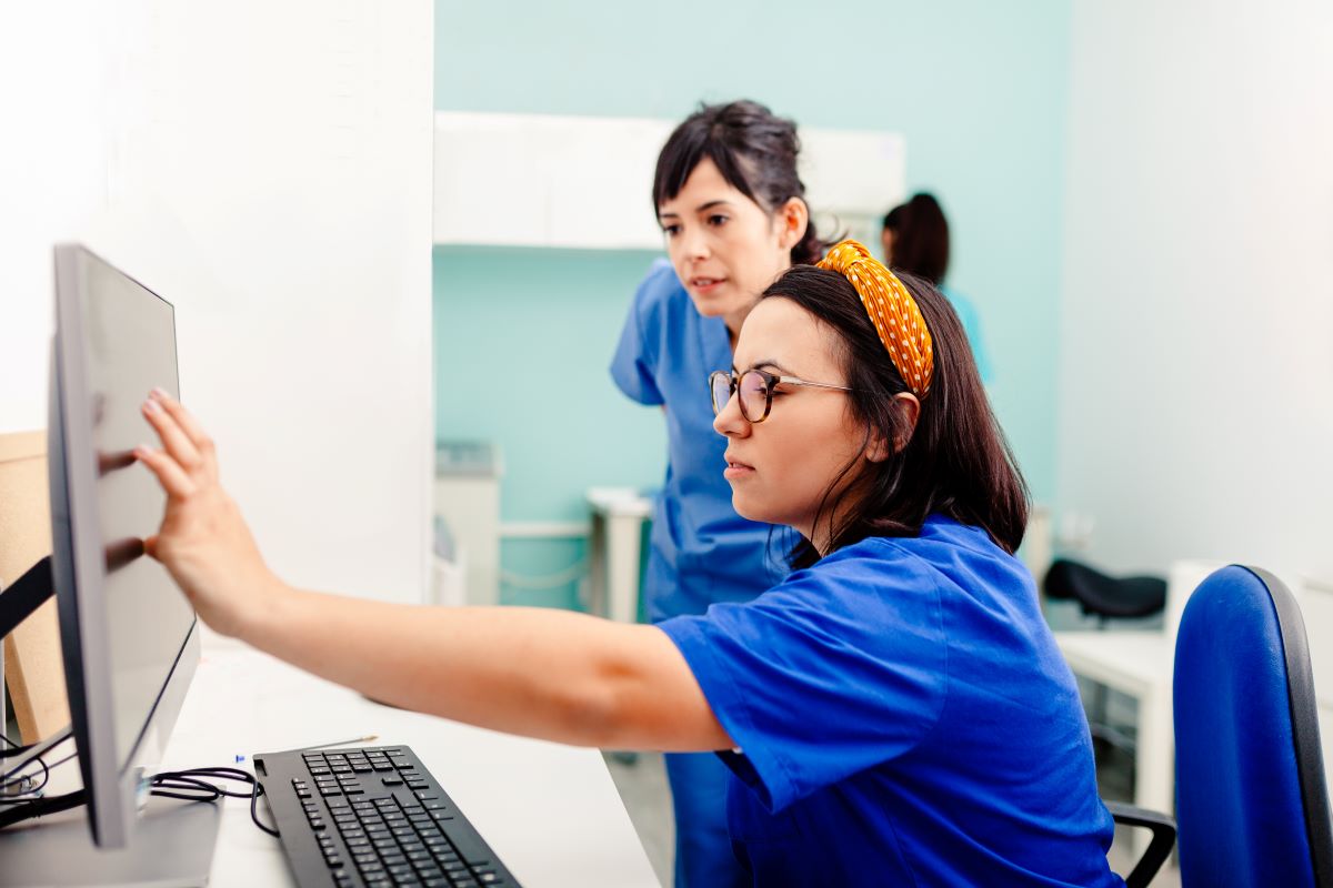 Two nurses discuss data on a computer screen.