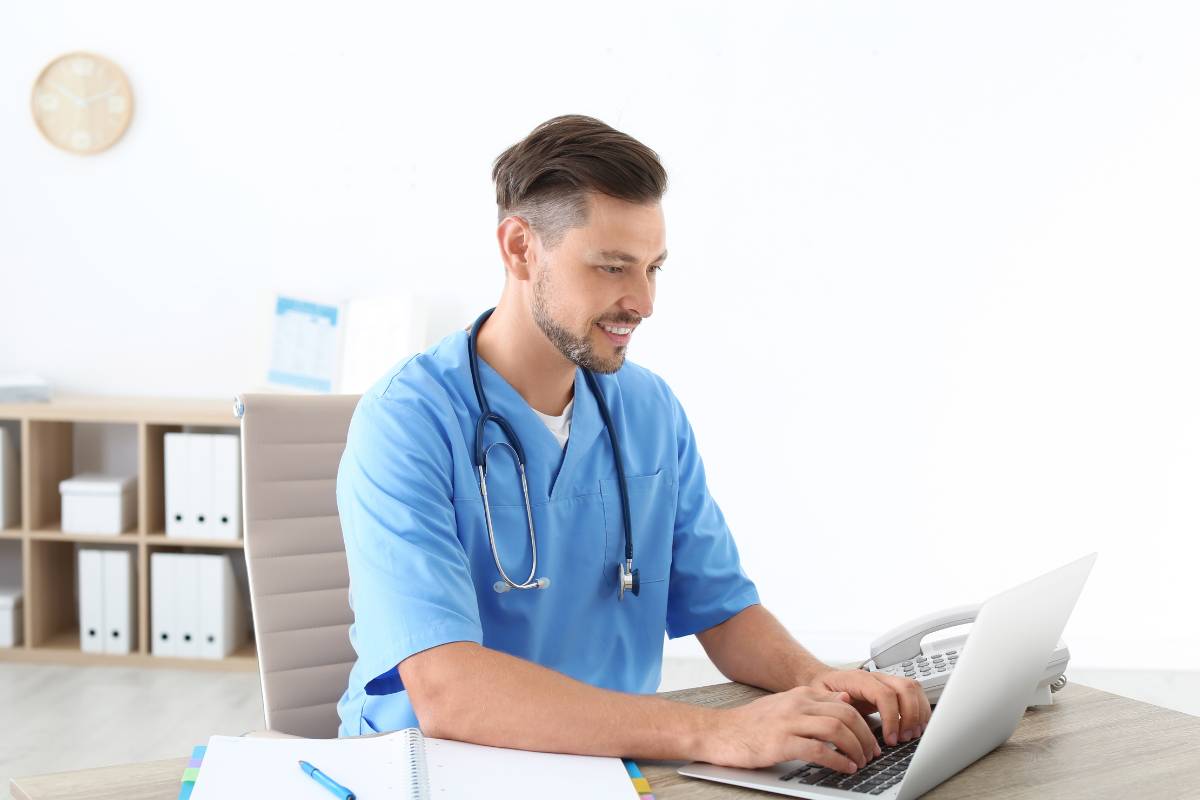 A nurse coder in blue scrubs works on a computer.