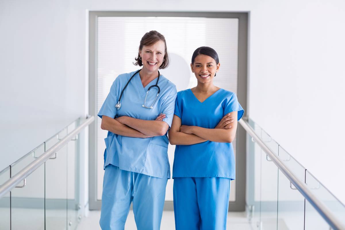 Two nurses stand in a hallway and demonstrate the answer to the question: What do nurses wear?