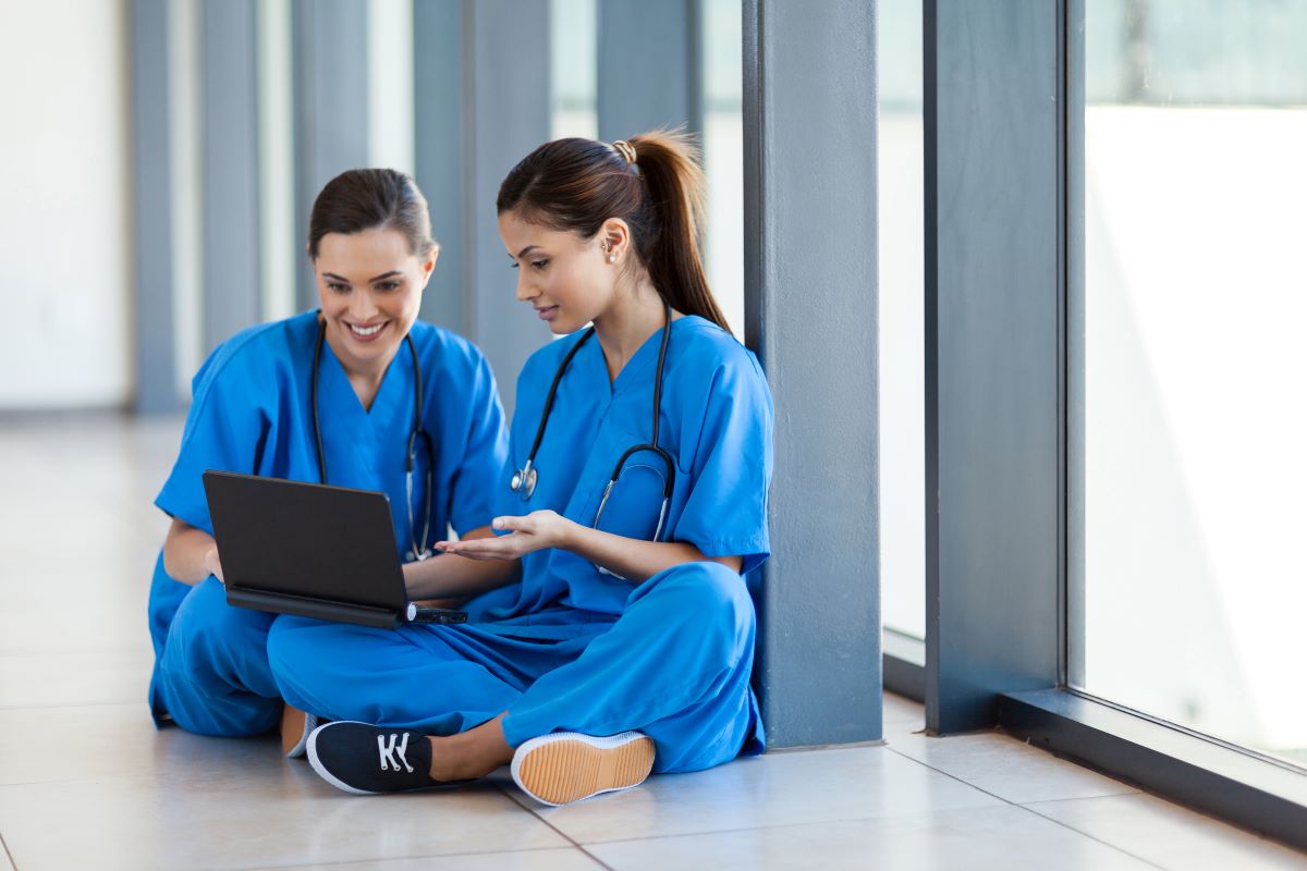 Two nurses sitting on the floor and looking at a laptop together.