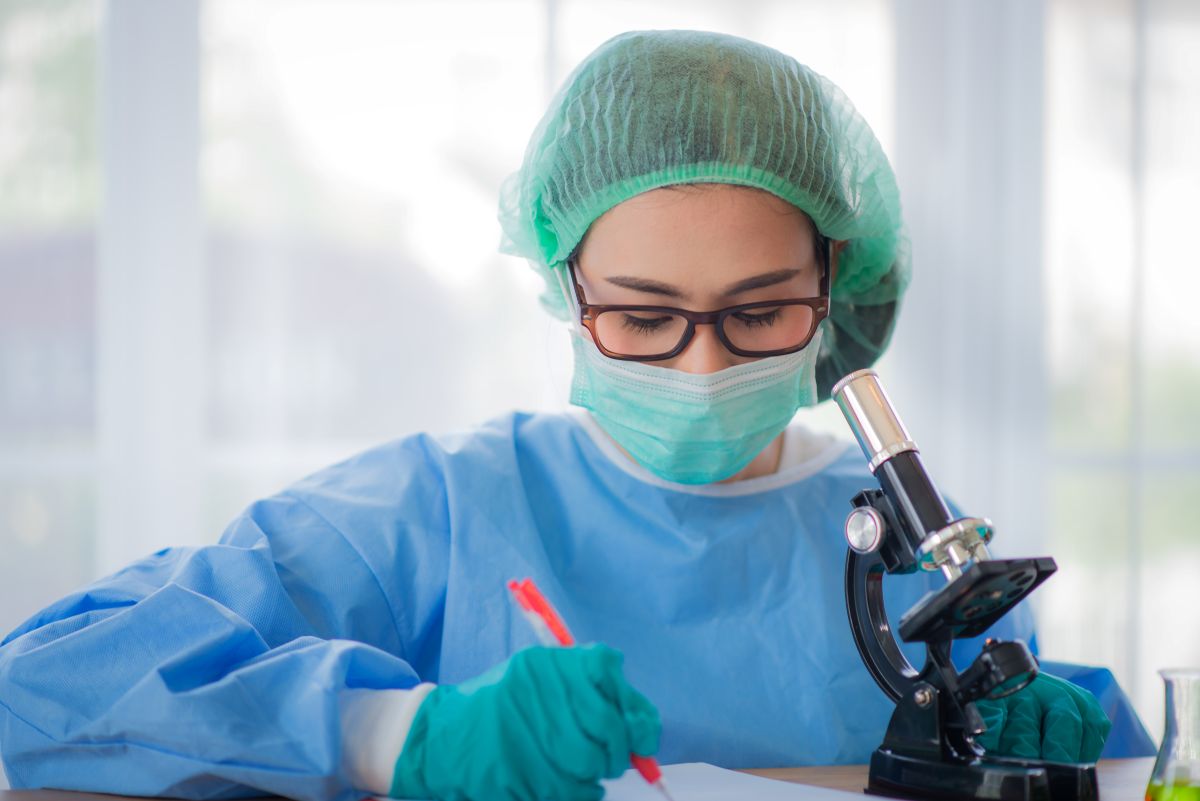 A research nurse takes notes based on what she's observing through a microscope.