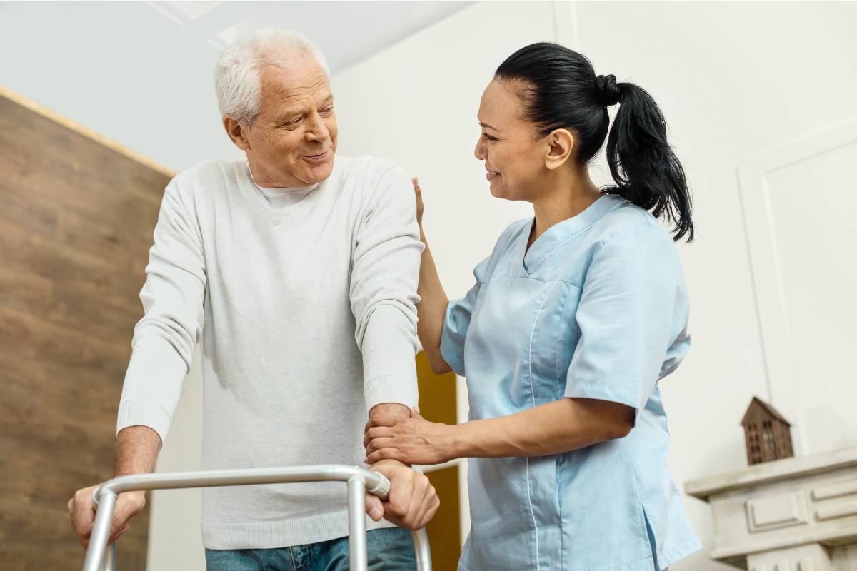 An adult gerontology nurse practitioner assists a patient with a walker.